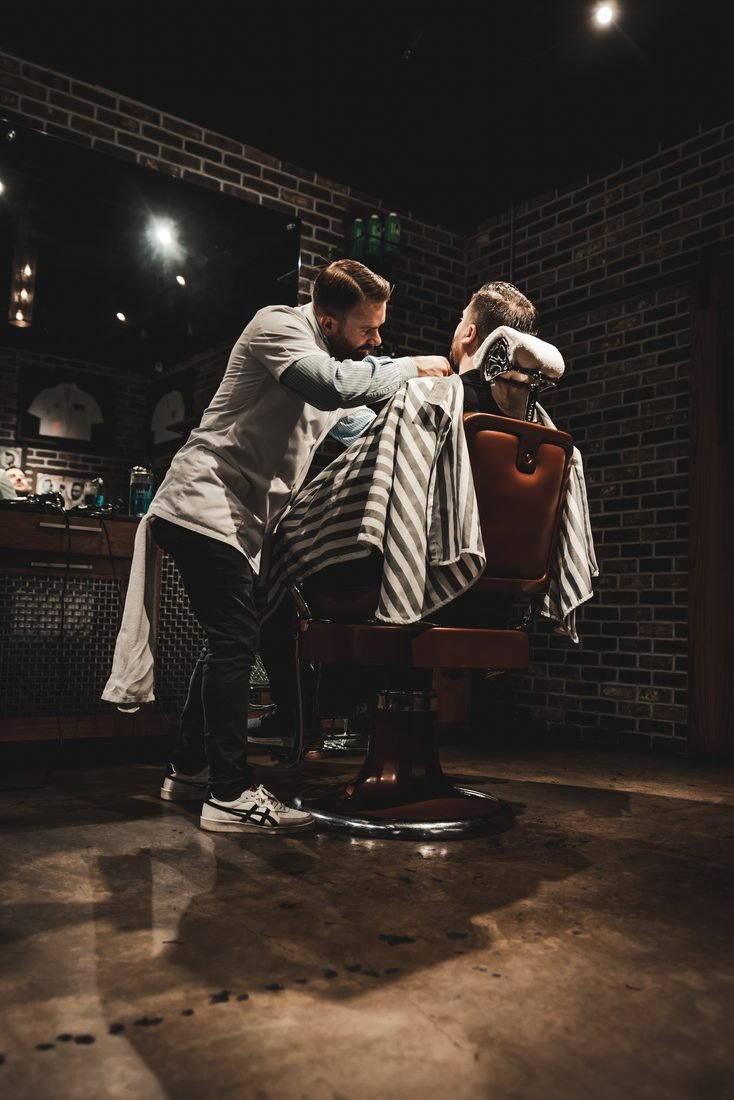 Barber laying a cape over a client in a dark barbershop